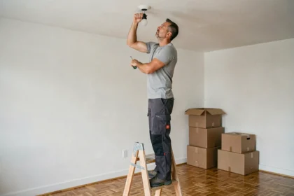 Homme installant un luminaire au plafond après un déménagement dans un salon vide avec des cartons