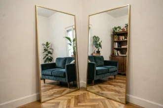 Grand miroir XXL appuyé contre un mur blanc dans un petit salon parisien, créant une illusion d'agrandissement de l'espace